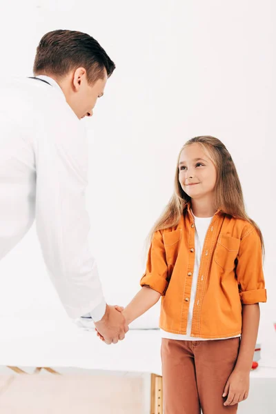 Pediatrist in white coat and child shaking hands and looking at each other — Stock Photo