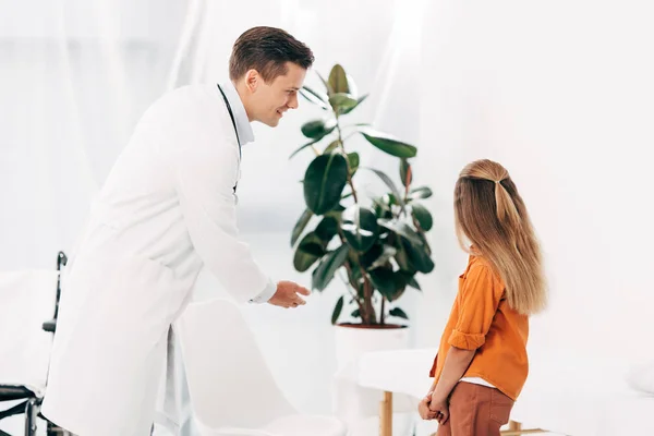 Pediatra sonriente y niño mirando la planta verde en la clínica - foto de stock