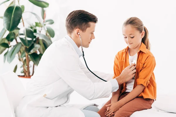 Pediatra de bata blanca examinando a un niño con estetoscopio - foto de stock