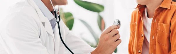 Plano panorámico de pediatra en bata blanca examinando niño con estetoscopio - foto de stock