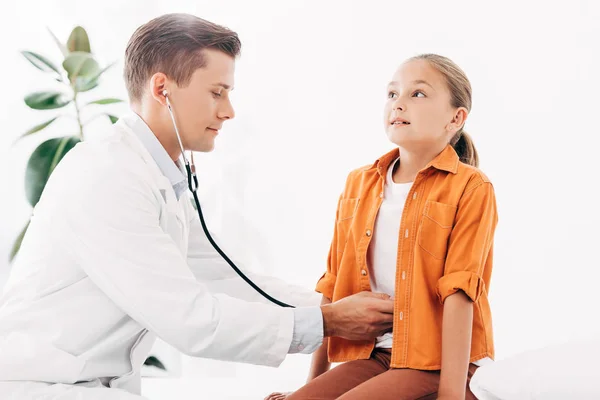 Педиатр в белом халате осматривает ребенка со стетоскопом — стоковое фото