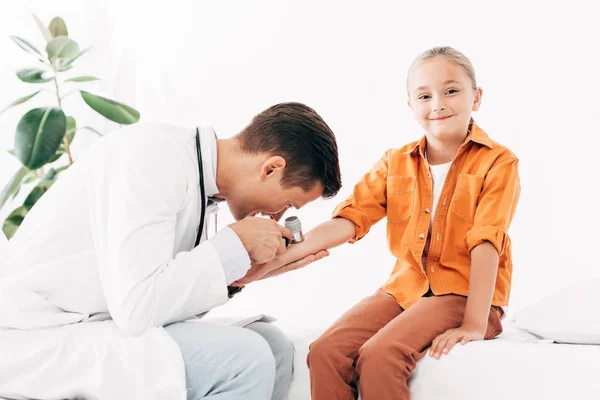 Pediatra enfocado en abrigo blanco examinando niño con dermascope - foto de stock