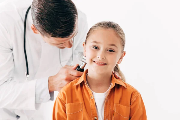 Pediatra focado em casaco branco examinando criança com dermascópio isolado em branco — Fotografia de Stock