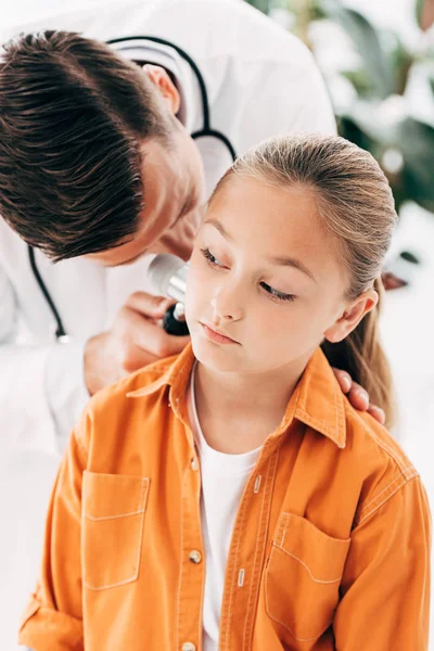 Pediatra enfocado en abrigo blanco examinando niño con dermascope - foto de stock