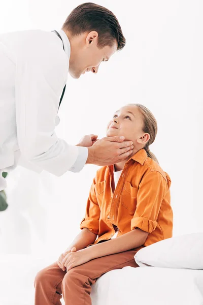 Pediatra sonriente con bata blanca examinando a un niño en la clínica - foto de stock