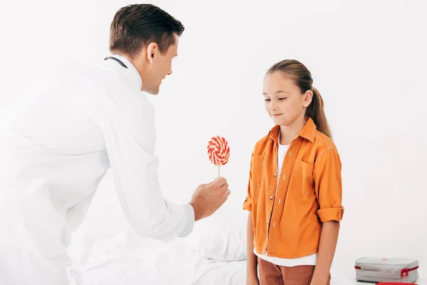 Pediatrist in white coat giving candy to child in clinic — Stock Photo