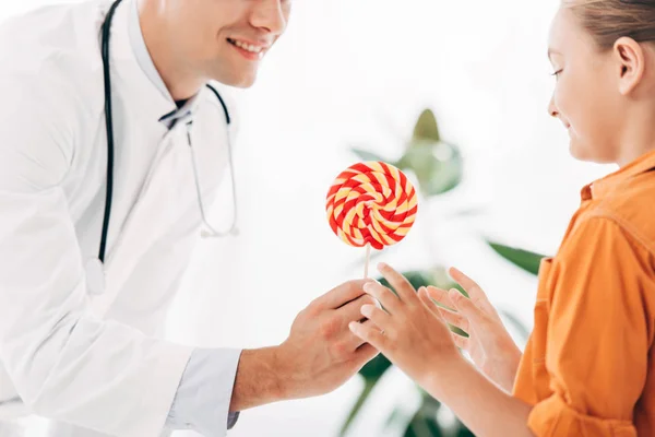 Vue partielle du pédiatre en manteau blanc donnant des bonbons à l'enfant à la clinique — Photo de stock