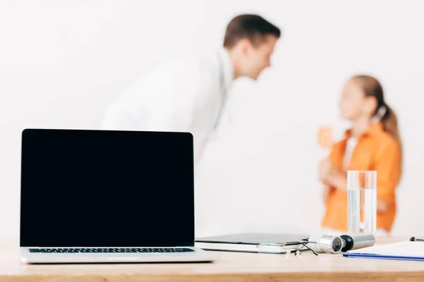 Selective focus of pediatrist and child and laptop with blank screen on foreground — Stock Photo