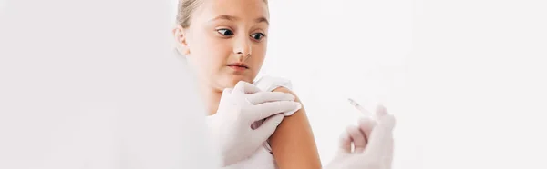Tiro panorâmico de pediatra em luvas de látex fazendo injeção a criança isolada em branco — Fotografia de Stock