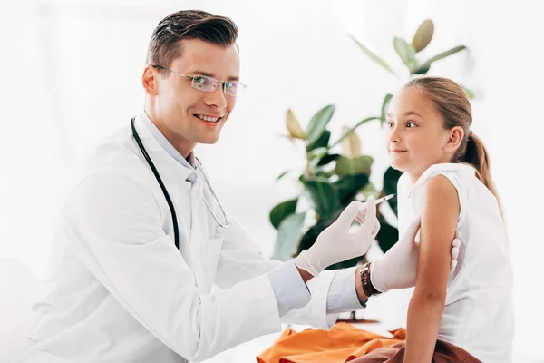 Smiling pediatrist in latex gloves doing injection to child — Stock Photo