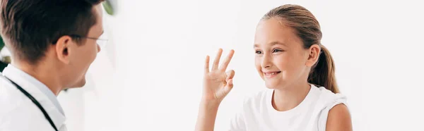 Plano panorámico de pediatra y niño sonriente mostrando signo de bien - foto de stock