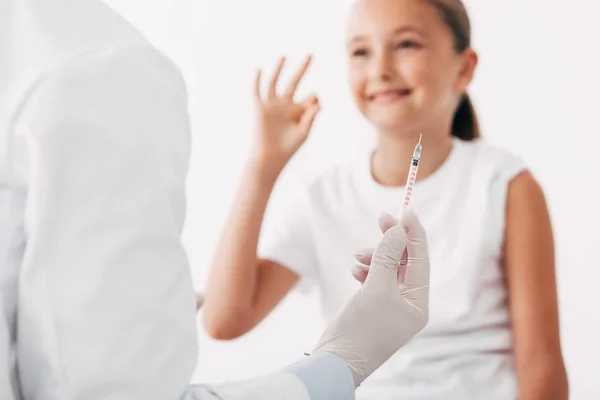 Partial view of pediatrist holding syringe and smiling child showing okay sign — Stock Photo