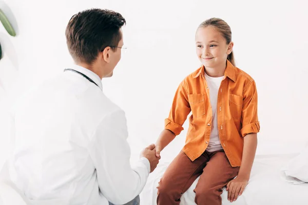 Pédiatre en manteau blanc et enfant serrant la main à la clinique — Photo de stock