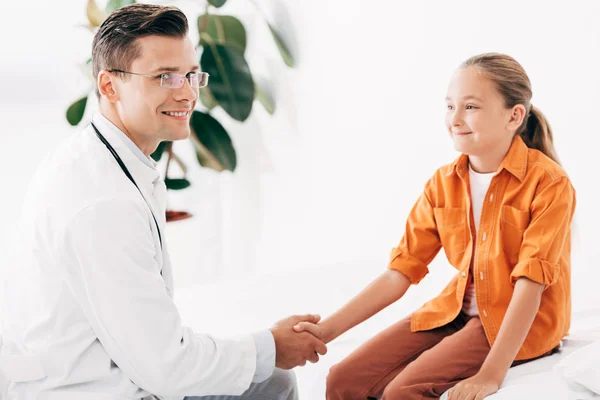 Pediatrist in white coat and child shaking hands in clinic — Stock Photo