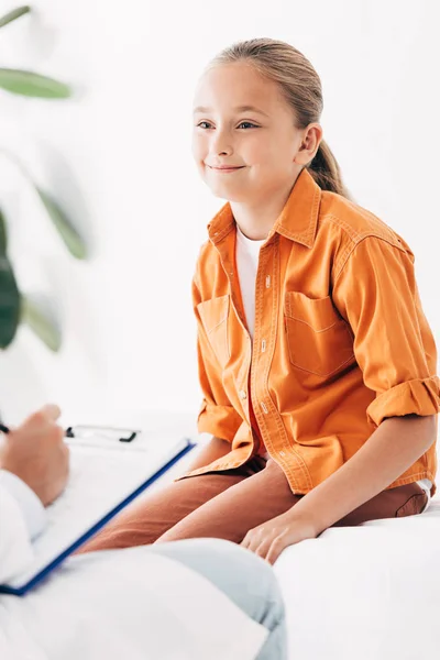 Partial view of pediatrist writing in clipboard while examining child in clinic — Stock Photo