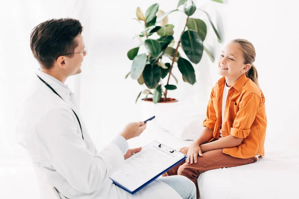 Pediatrist holding clipboard while examining child in clinic — Stock Photo