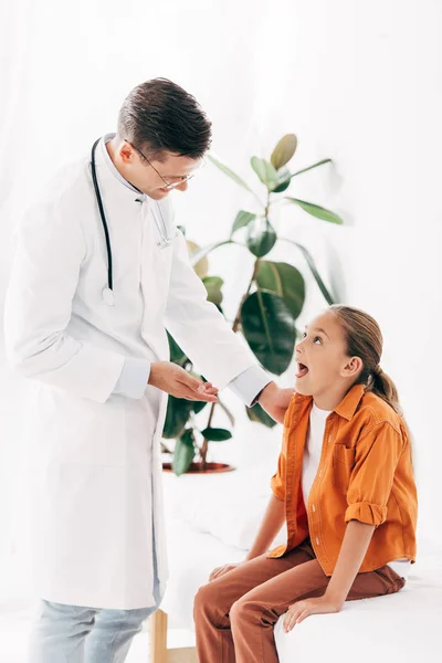 Pédiatre souriant en manteau blanc et enfant à la clinique — Photo de stock