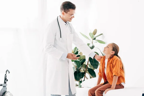 Smiling pediatrist in white coat and child looking at each other in clinic — Stock Photo