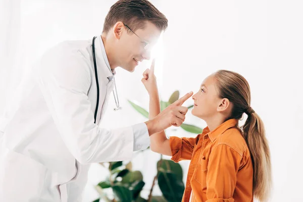 Pediatra sorridente in camice bianco e bambino che si guarda in clinica — Foto stock