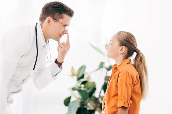 Smiling pediatrist in white coat and child looking at each other in clinic — Stock Photo