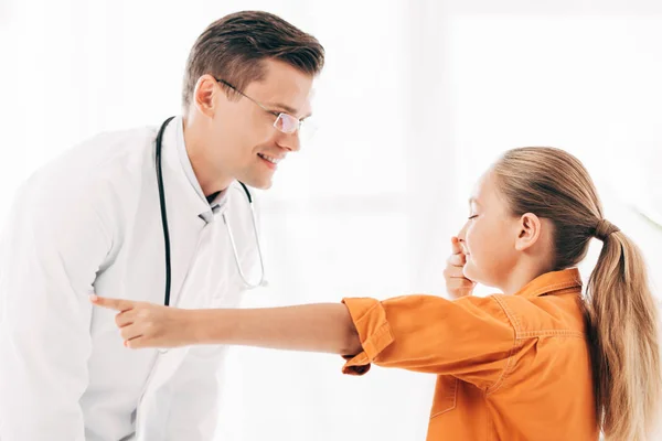 Pediatra sorridente in camice bianco e bambino che tocca il naso in clinica — Foto stock