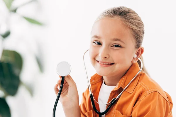 Bambino sorridente che tiene lo stethscope e guarda la fotocamera in clinica — Foto stock