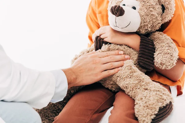 Vue partielle du pédiatre en manteau blanc et enfant avec ours en peluche isolé sur blanc — Photo de stock