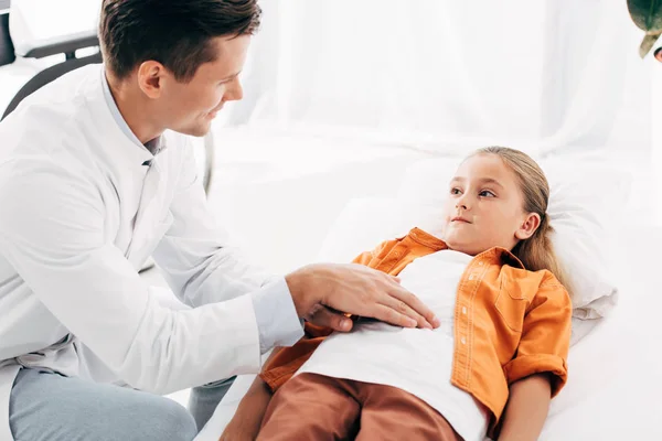 Pédiatre souriant en manteau blanc examinant l'enfant à la clinique — Photo de stock