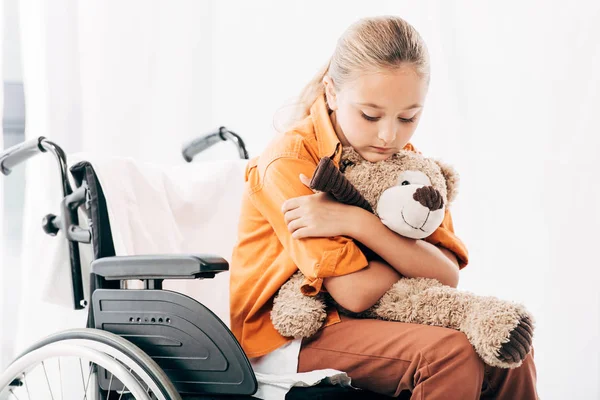 Pensive kid holding teddy bear and sitting on wheelchair — Stock Photo