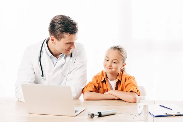 Smiling pediatrist in white coat and child using laptop in clinic — Stock Photo