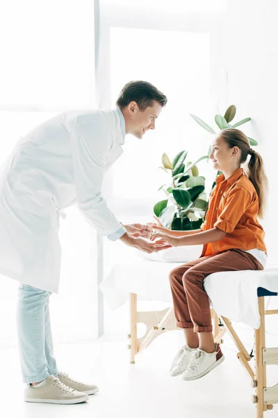 Smiling pediatrist in white coat giving glass of water to child in clinic — Stock Photo