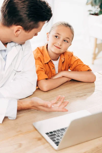 Pediatrist in white coat and child using laptop in clinic — Stock Photo