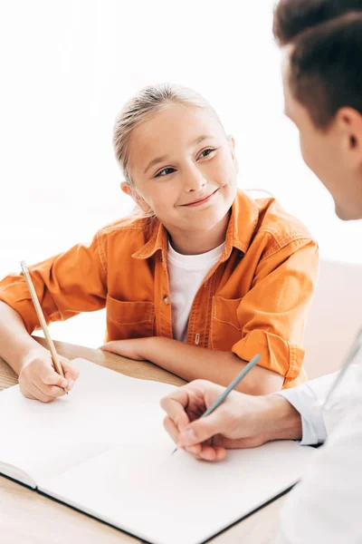 Smiling child and pediatrist writing in notebook at table in clinic — Stock Photo