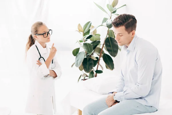 Criança em óculos e traje médico examinando paciente — Fotografia de Stock