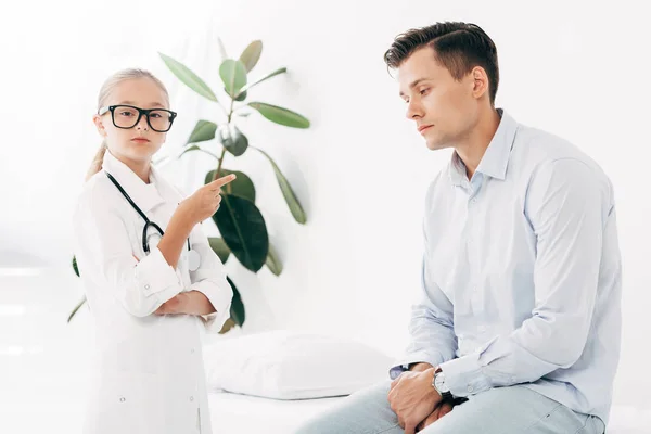 Niño en gafas y traje médico examinando paciente - foto de stock