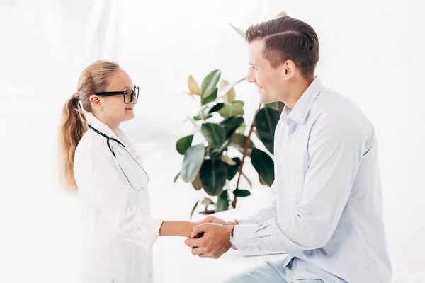 Усміхаючись дитиною в доктора костюм тримає руки з пацієнтом — стокове фото