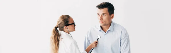 Tiro panorâmico de criança em traje médico examinando paciente com estetoscópio isolado em branco — Fotografia de Stock