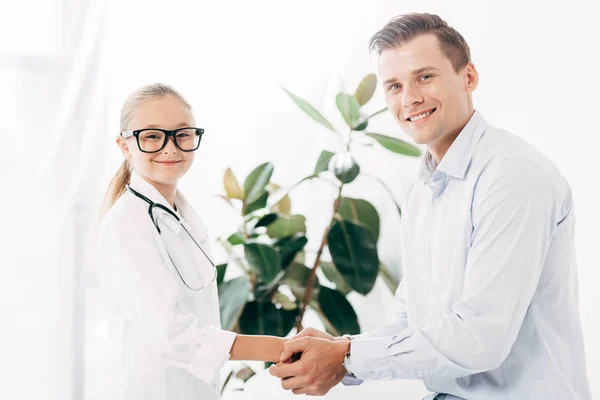 Smiling kid in doctor costume holding hands with patient — Stock Photo