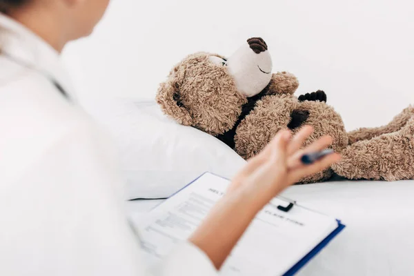 Partial view of child in doctor costume examining teddy bear — Stock Photo