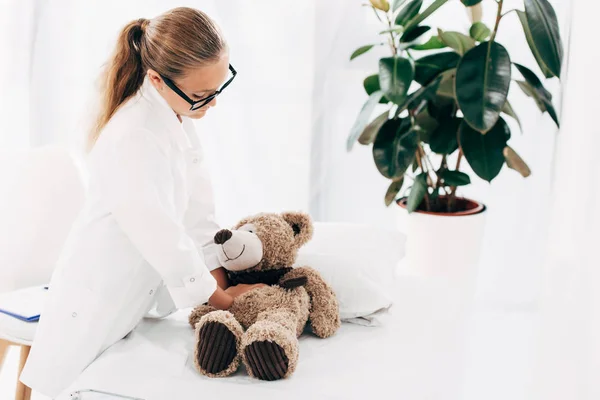 Kid in doctor costume doing heart massage to teddy bear — Stock Photo