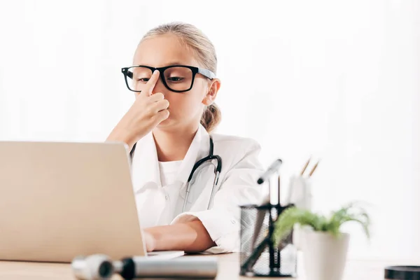 Criança em traje médico usando laptop na clínica — Fotografia de Stock