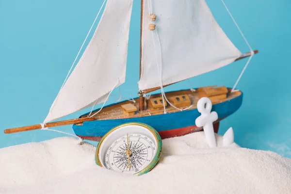 Close up view of decorative ship near anchor and compass in white sand isolated on blue — Stock Photo