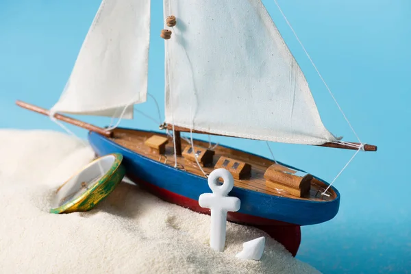 Navio em miniatura perto de bússola e âncora em areia branca isolada em azul — Fotografia de Stock