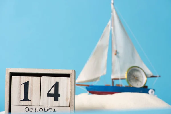 Calendrier en bois avec 14 Octobre date près du navire décoratif et boussole en sable blanc isolé sur bleu — Photo de stock