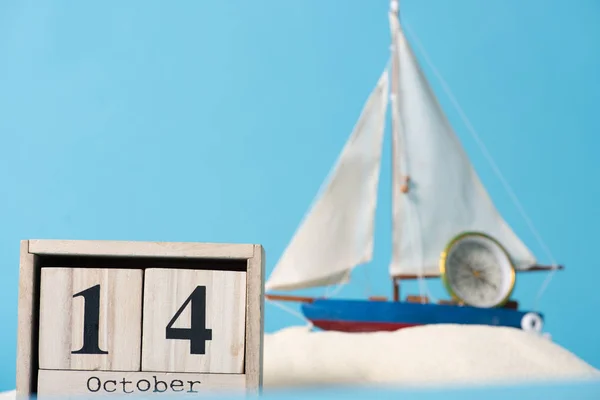 Wooden calendar with 14 October date near decorative ship and compass  in white sand isolated on blue — Stock Photo