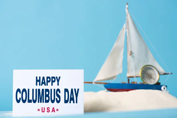 Card with happy Columbus Day inscription near miniature ship in white sand isolated on blue — Stock Photo