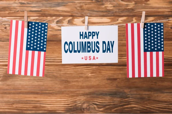 Card with happy Columbus day inscription between American national flags on wooden surface — Stock Photo