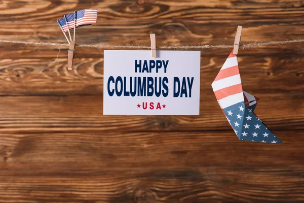 Carta con iscrizione felice Columbus giorno tra bandiere nazionali americane e barca di carta su superficie di legno — Foto stock