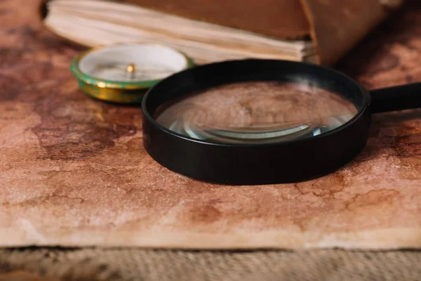 Close up view of magnifying glass near compass on aged world map — Stock Photo