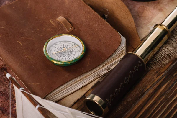 Compass on copy book with leather cover near telescope on wooden surface — Stock Photo